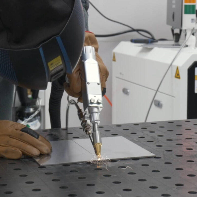 Spawanie laserowe metalowych elementów za pomocą ręcznego narzędzia laserowego na stole roboczym — Wsparcie Laserowe.