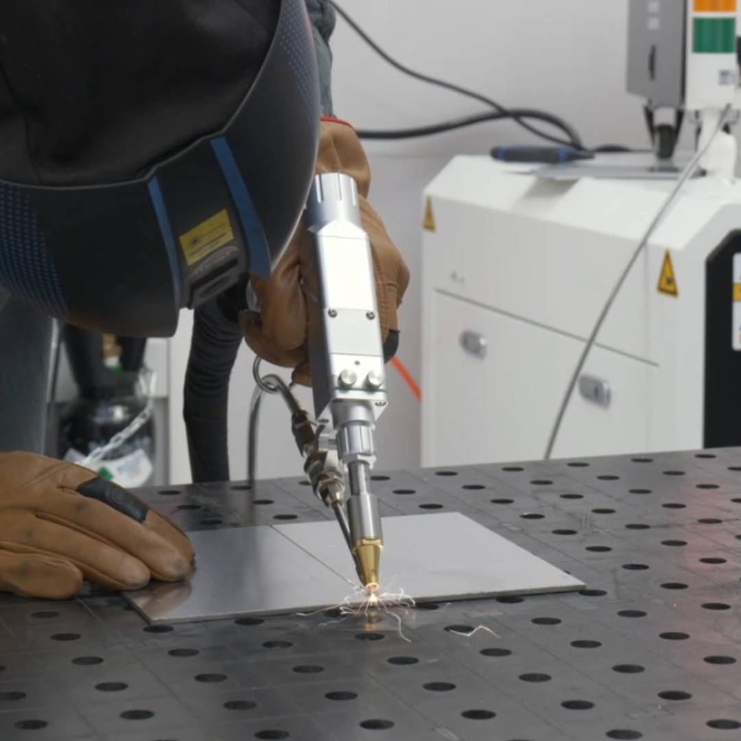 Spawanie laserowe metalowych elementów za pomocą ręcznego narzędzia laserowego na stole roboczym — Wsparcie Laserowe.
